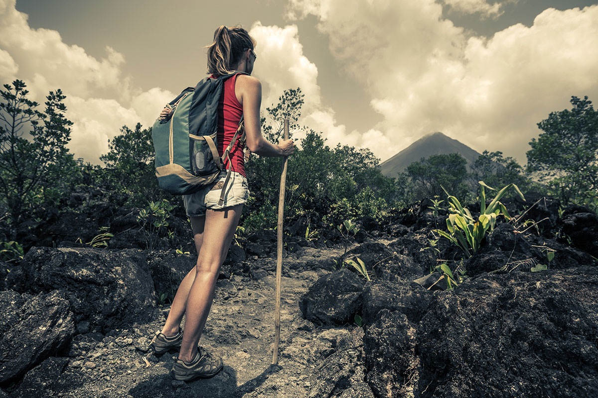 A woman enjoys a hike and admires a volcano in the distance.
